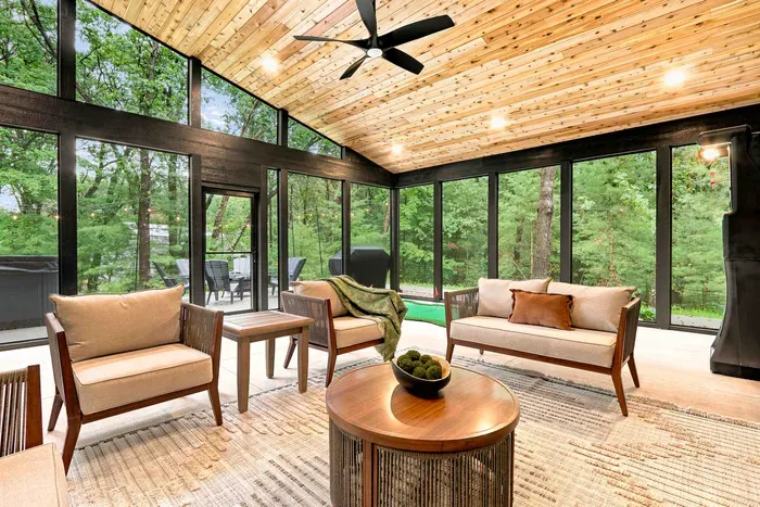 Screened-in patio with cozy lounge seating, ceiling fan, and peaceful wooded views for relaxing in every season.