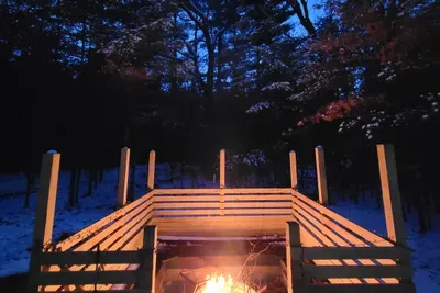 Cozy up by the fire under a winter-blue sky, with snow-dusted woods creating a peaceful, cabin-style escape.