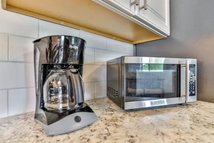 Convenient kitchen countertop setup featuring a coffee maker, microwave, subway tile backsplash, and clean, functional prep space.