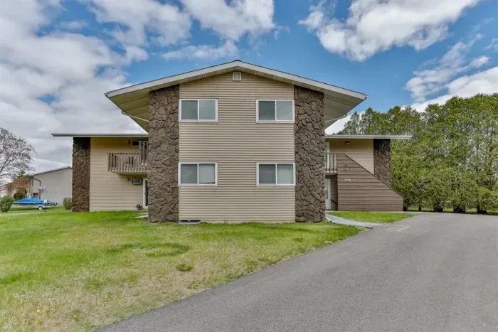Attractive apartment exterior with stone accents, green lawn space, and convenient parking access.