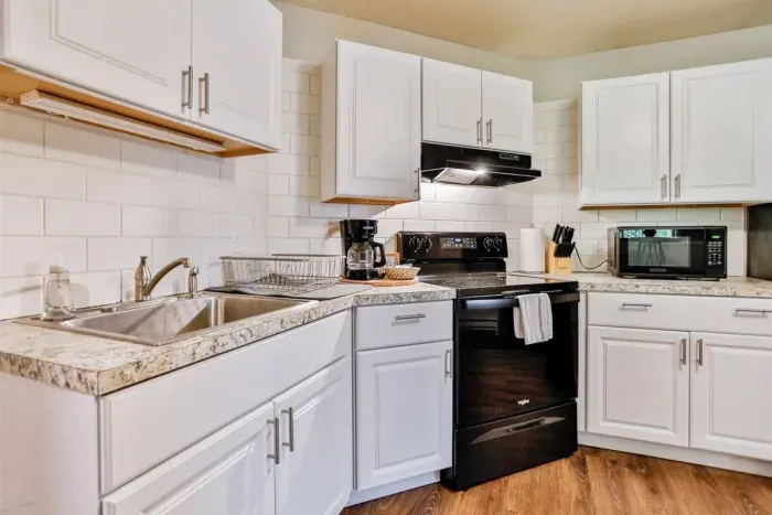 A modern kitchen equipped with high-end appliances and ample lighting. It has a coffee maker, oven, stove top, utensils, and all it takes to fix a delicious meal.