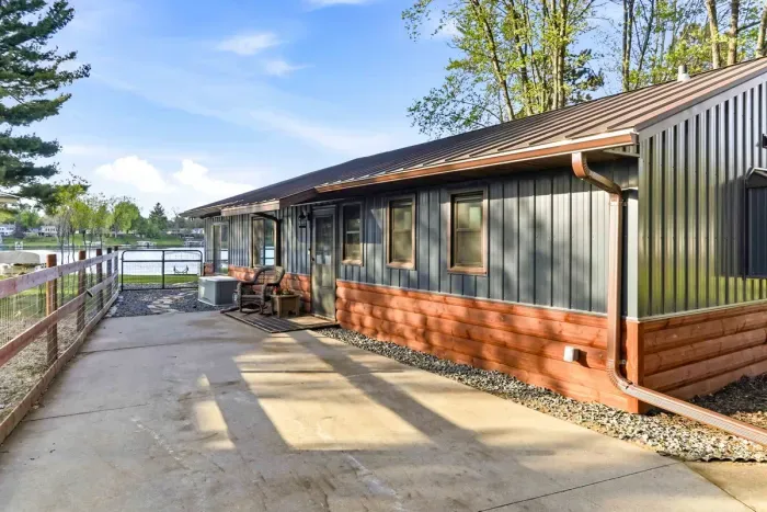 Lakeside cottage exterior with a spacious patio, updated metal siding, and peaceful water views just steps away.