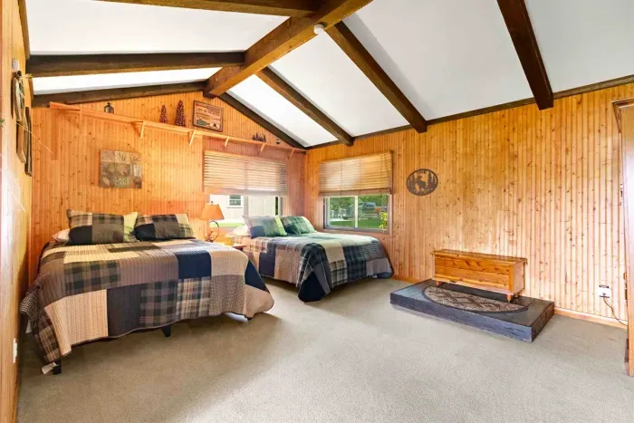 This cozy room features two comfortable beds nestled against warm wooden walls, creating a rustic and inviting atmosphere.