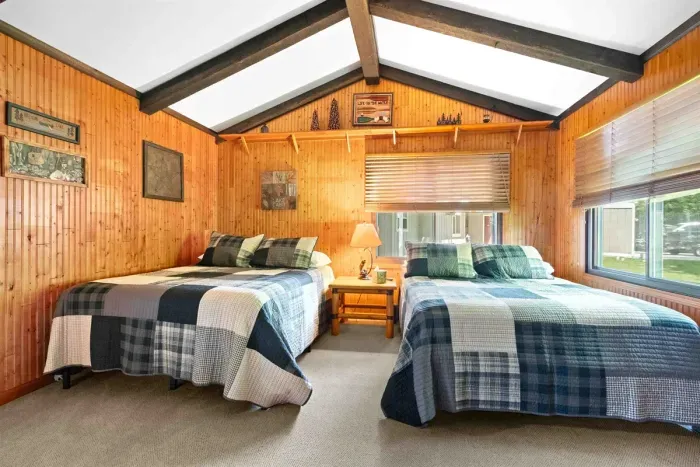 This cozy room features two comfortable beds nestled against warm wooden walls, creating a rustic and inviting atmosphere.