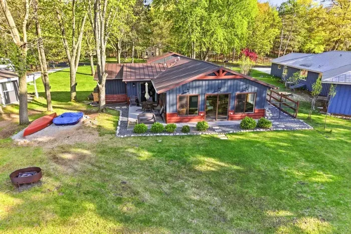 Scenic aerial shoreline view showcasing a sandy beach area, dock access, and a spacious green lawn leading back to the cottages.