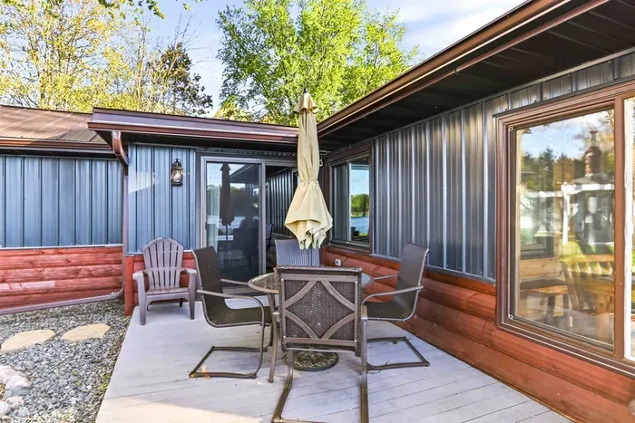 Charming cottage exterior featuring updated siding, a relaxing patio area, and a peaceful green setting near the lake.
