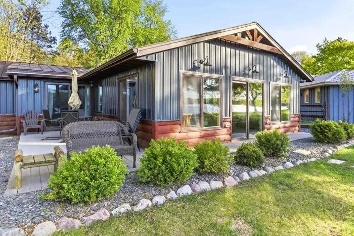 Modern lakeside cottage exterior with outdoor seating, landscaped grounds, and peaceful water views just beyond the patio.