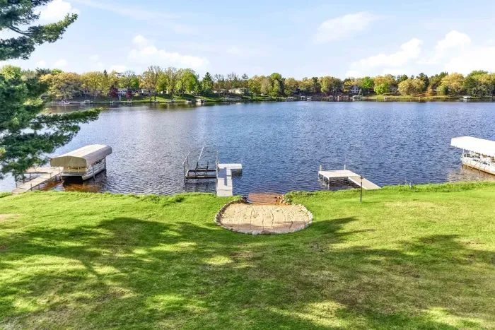 Beautiful lakefront view with open green space, sandy shoreline access, and docks for enjoying the water.