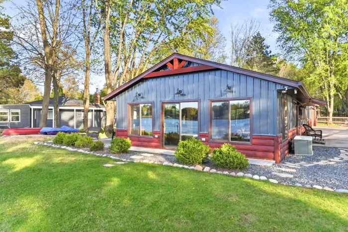 Modern lakeside cottage exterior with large picture windows, landscaped grounds, and beautiful lake views from the lawn.