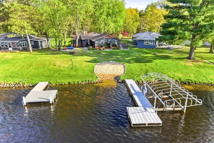 Expansive lakefront grounds with a sandy swim area, dock access, and a peaceful cottage setting surrounded by greenery.