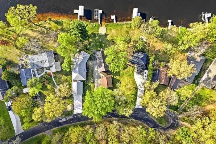 Overhead aerial view showcasing the lakefront neighborhood, tree-filled lots, private docks, and direct shoreline access.