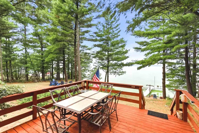 Dine al fresco at the outdoor dining table with seating on this elevated wooden deck, offering breathtaking lake views through a canopy of peaceful pine trees.