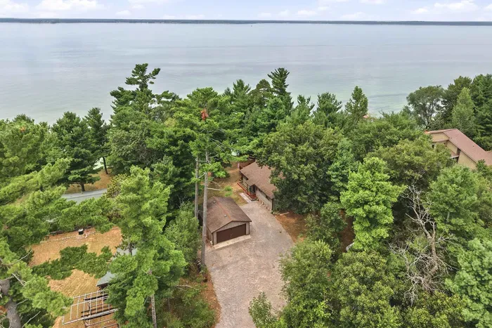 Escape to a secluded lakeside retreat nestled in a lush pine forest, featuring a detached garage and a spacious gravel driveway with endless open-water views just beyond the trees.