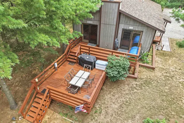 Host unforgettable outdoor gatherings on this expansive, multi-tier wooden deck, complete with an outdoor dining table, comfortable seating, and a gas grill surrounded by peaceful pine trees.