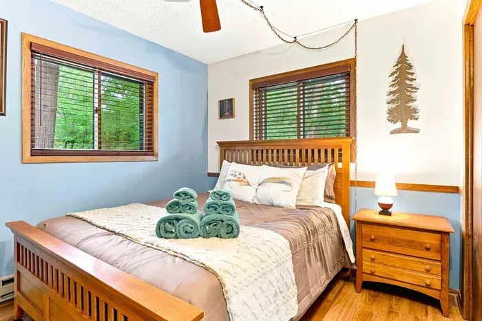 Unwind in a serene, nature-inspired bedroom anchored by a solid wood bed and warm bedside lighting from the nightstand with drawers. Enjoy serene tree-lined views right from bed as you ease into vacation mode.