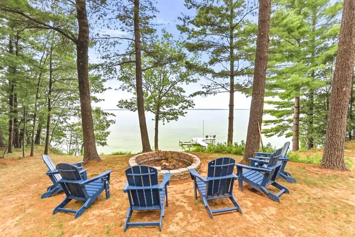 Gather under towering pines around the stone fire pit with comfortable Adirondack chairs for cozy evenings, panoramic lake views, and pure relaxation right along the shore.