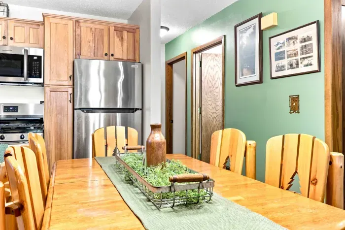 Gather around the crafted wooden dining table with pine-accent chairs for memorable group meals and lively conversations. Steps away from the open kitchen outfitted with a stainless steel refrigerator, gas stove, and microwave, serving up delicious food.