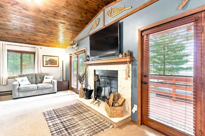 Sink into comfortable seating in this rustic, open-concept lounge highlighted by a wood-burning fireplace and a wall-mounted flat-screen TV. Expansive glass doors frame picturesque lake views and provide direct access to the outdoor deck.