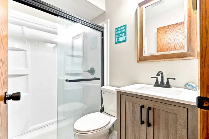 Refresh and recharge in this updated bathroom featuring a spacious walk-in shower with glass doors. A sleek single-sink vanity with modern matte black fixtures and a rustic wood-framed mirror offer the perfect space to get ready for a day on the lake.