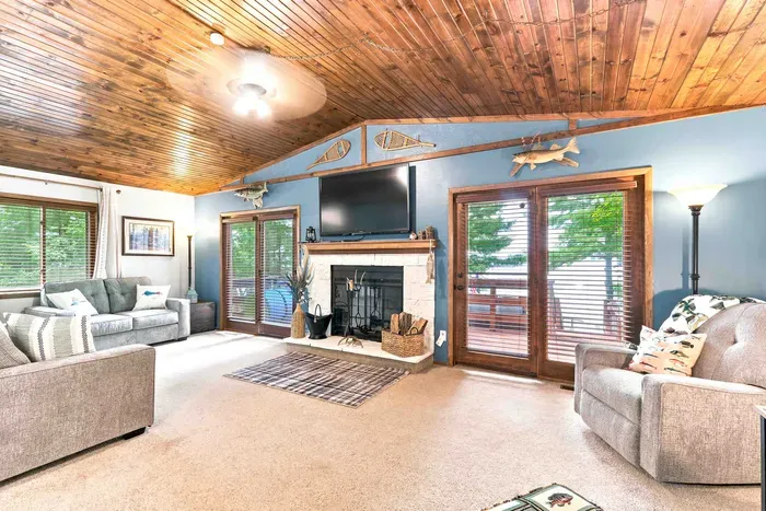 Relax in a light-filled living area beneath soaring wood ceilings and a gentle breeze from the ceiling fan. Gather around the classic stone fireplace for cozy evenings, stream movies on the flat-screen TV, or step through sliding glass doors to enjoy.