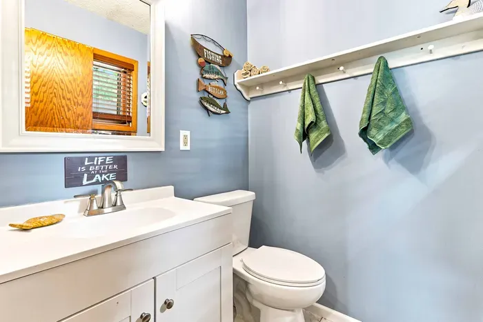 Freshen up in this charming half-bath featuring soft lake-house blue walls, a clean white vanity with storage, and a large wall mirror. Complete with a convenient towel rack with hooks and playful nautical decor, it’s a sweet, practical spot to gear up.