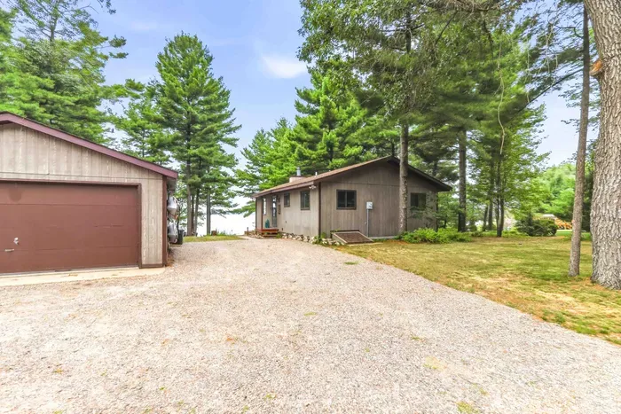 Arrive at your peaceful lakeside retreat, nestled among towering pine trees with glimpse of the water just beyond. Featuring a large gravel driveway for easy parking and vehicle access, a spacious detached garage, and wall-mounted kayaks ready for you.