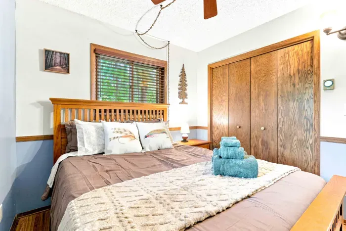 Rest up for another day on the lake in this cozy bedroom featuring a wooden frame bed, soft linens, and fresh plush towels. Dual windows bring in natural light, while an overhead ceiling fan ensures a cool, peaceful night's sleep.