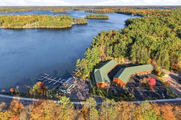 Your lakeside getaway awaits! Aerial view showing the lodge complex, lush pine trees, autumn colors, and surrounding water.