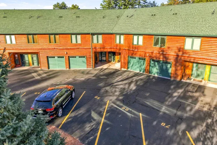 Classic cabin charm meets modern convenience. The multi-unit lodge features rich log siding, forest-green roofing, matched garage doors, and designated parking spots right outside your door for maximum convenience during your stay.