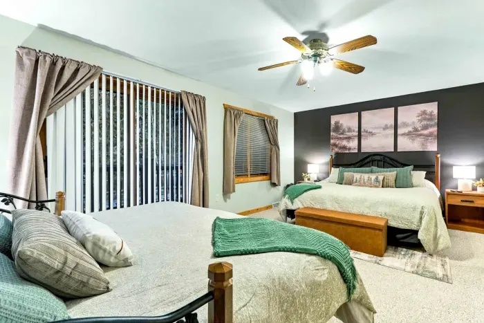 Ideal for families or groups, this airy bedroom offers two plush beds accented with warm earth tones and sage green bedding. Large windows and sliding glass doors fill the space with natural light while providing seamless outdoor access.