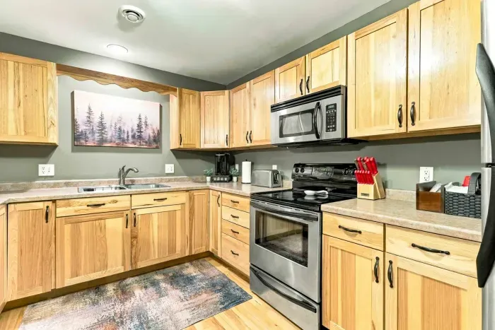 Warm natural wood tones combine with sleek stainless steel appliances to create an inviting cooking space. Featuring a smooth-top range, built-in microwave, and spacious refrigerator, you'll have everything needed to feel right at home.