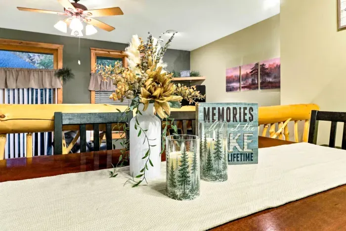 It’s all about the thoughtful touches! The dining table is styled with a neutral table runner, a white ceramic vase filled with dried botanicals, pine-printed glass hurricane candles, and a sweet "Memories Made at the Lake Last a Lifetime" sign.