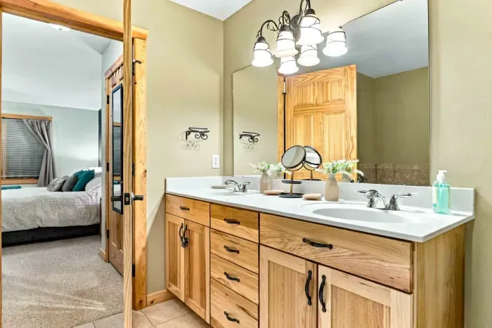 Streamline your morning routine with a spacious double-sink vanity featuring modern white countertops and natural oak cabinetry. Complete with a large vanity mirror, rustic light fixtures, and plentiful drawer storage.