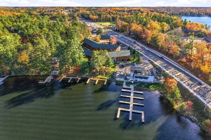 Experience the pinnacle of lakeside living! This high-altitude aerial view showcases the property’s enviable location right on the shore, featuring extensive private boat docks, direct water access, and vibrant autumn foliage lining the lakefront.