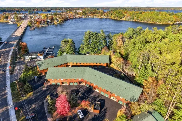 Experience the charm of a true lakeside escape. This bird's-eye view highlights the classic timber-clad lodge design, surrounding pine canopy, pop of fall foliage, and quick access to nearby water activities.