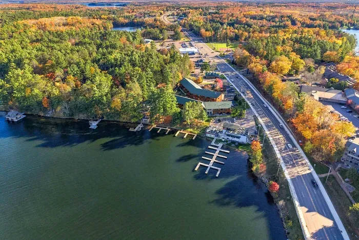 Where forest meets the shore. From broad lake views to lush pine and autumn canopies, this bird's-eye perspective highlights the property's expansive waterfront dock system, pristine waters, and nearby scenic roadways.