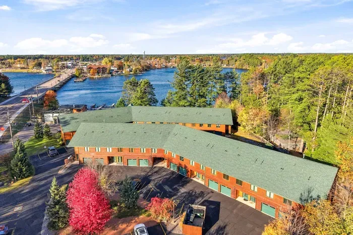 Take in the stunning aerial view of this lakeside retreat nestled among lush evergreens and vibrant autumn foliage. Featuring classic wood-siding architecture, green roofing, and generous parking, this sprawling property offers a picturesque setting right