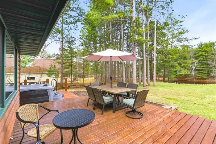 Cozy cabin-style backyard patio with dining table, umbrella, and forest views.