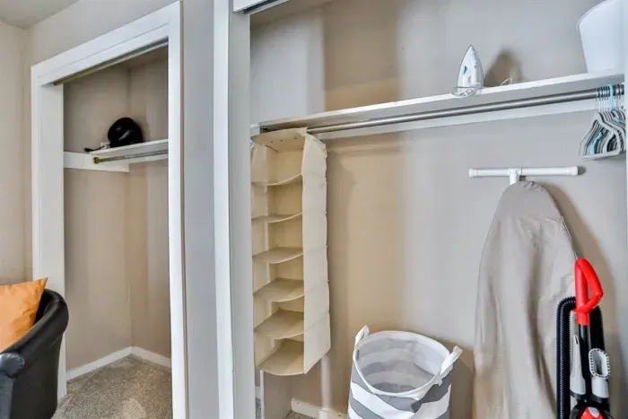 An open closet with shelves and hanging rods, showing organized storage items like hangers, a fabric organizer, a laundry basket, and a vacuum cleaner.
