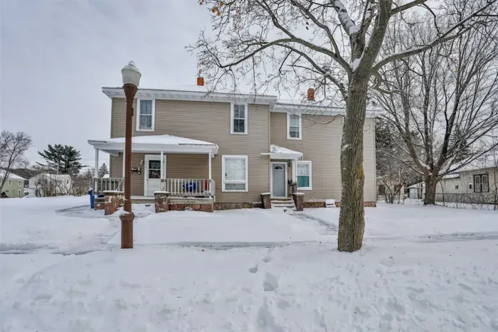 The house features a beige exterior with white trim, and a covered porch in the front with a railing.