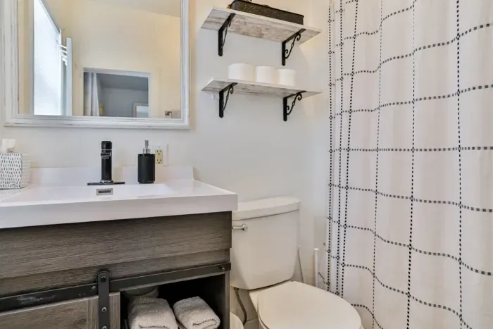 Bright bathroom featuring a modern vanity, shower, and open shelving.