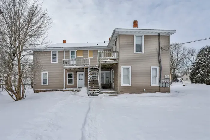 Rear view of a multi-unit home featuring neutral siding, upper-level balconies, exterior stair access, showing a well-kept, functional layout.