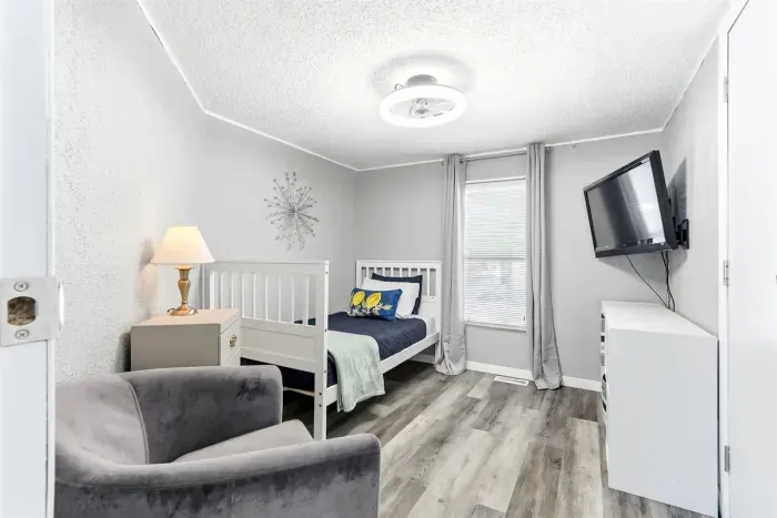 Cozy bedroom featuring a comfortable bed, a seating couch, wall-mounted TV, and soft lighting from a stylish lampshade.