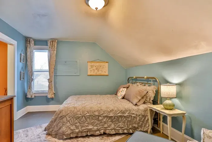 Kid's bedroom with soft blue walls, a comfortable bed, and warm lighting. Features charming decor, and a bedside table with lamp.