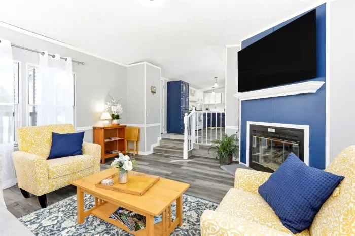 Modern living room with vibrant yellow chairs, a blue-accented fireplace, and open access to a sleek kitchen.