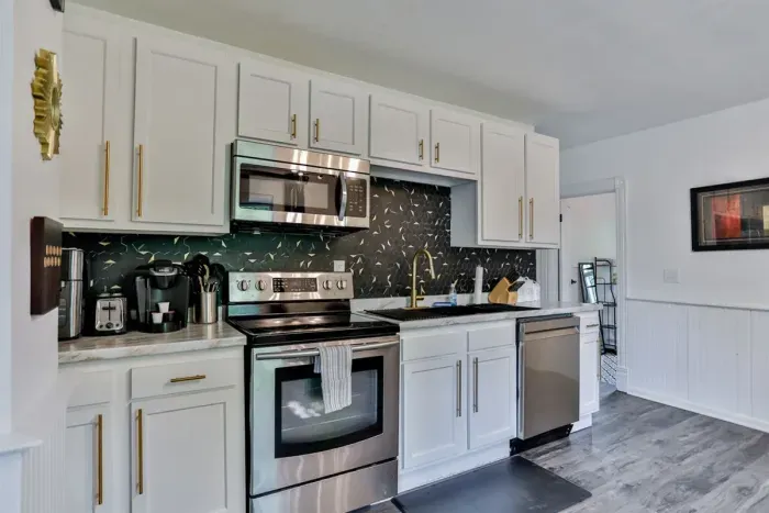 A modern kitchen equipped with high-end appliances and ample lighting. It has a coffee maker, oven, stove top, utensils, and all it takes to fix a delicious meal.