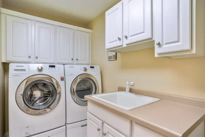 The shared laundry room features convenient top cabinetry and a built-in lavatory, offering a practical and well-organized space for everyday needs.