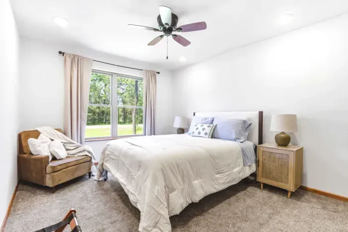 Rest easy in a bright, peaceful bedroom with soft textures, cozy seating, and calming views of the trees.