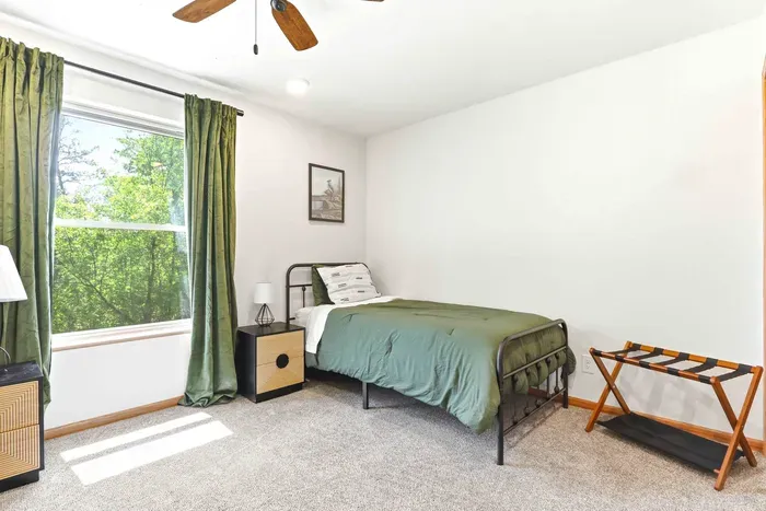 Rest easy in a cozy, light-filled bedroom with calming green tones and peaceful treetop views.