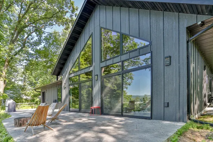 Enjoy indoor-outdoor living with outdoor patio seating and a grill, all set beside striking floor-to-ceiling windows and peaceful wooded views.